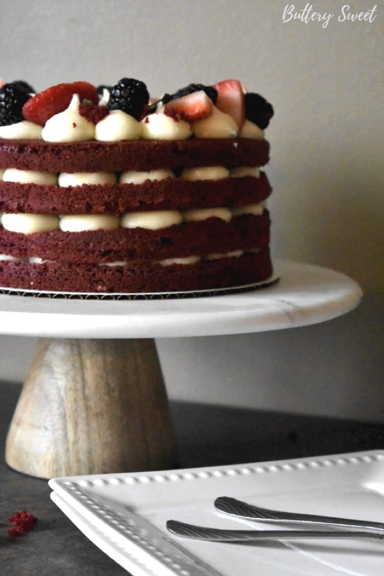 Easy Red Velvet Cake on cake stand with layers of frosting and berries 