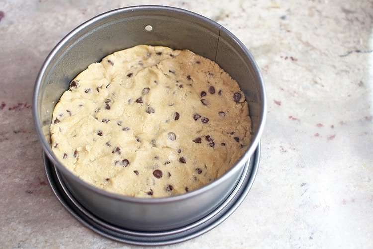 raw cookie dough pressed into springform pan for crust of Instant Pot Chocolate Chip Cookie Dough Cheesecake