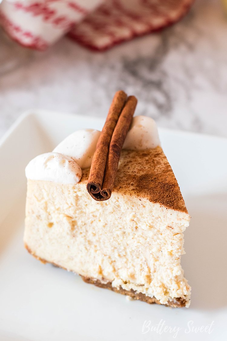 slice of Instant Pot Eggnog Cheesecake dusted with cinnamon and garnished with cinnamon stick on white plate