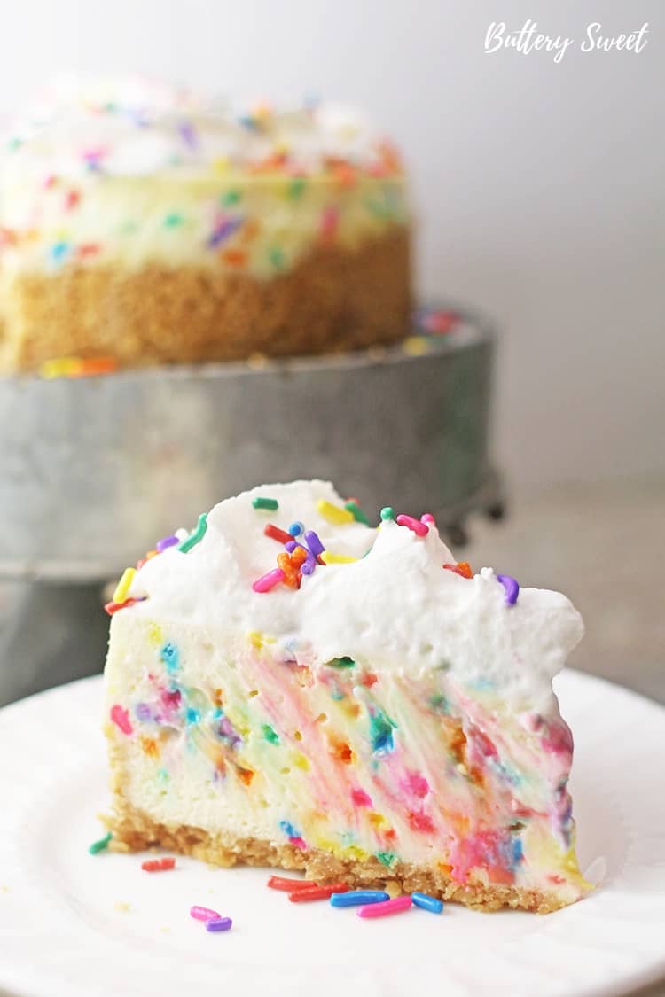 Slice of funfetti cheesecake on a white plate with the rest of the cheesecake in the background
