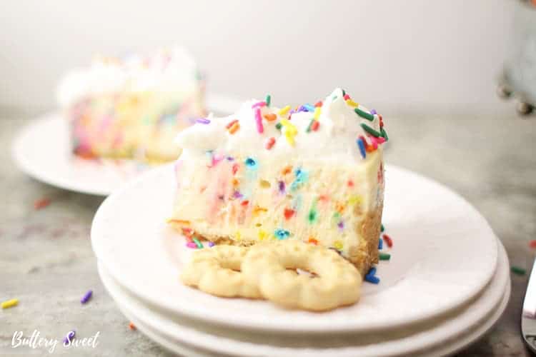 Slice of funfetti cheesecake on a stack of white plates with 2 butter cookies next to it.
